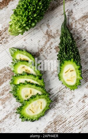 Blick auf einige rohe Karelascheiben, auch als bittere Melone oder bittere Kürbisse bezeichnet, auf einem weißen rustikalen Holztisch Stockfoto