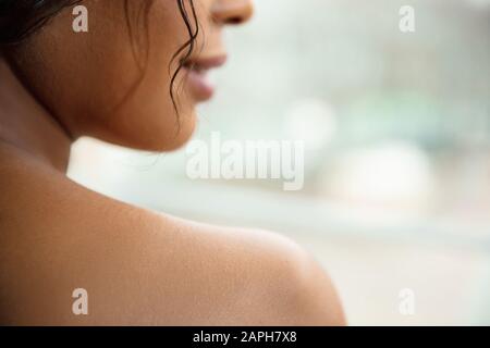 Beauty Day. Zärtlichkeit. Nahaufnahme der afroamerikanischen Frau, die auf Seite schaut und lächelt und die Schulter mit gesunder und gepflegter Haut zu Hause zeigt. Konzept von Schönheit, Selbstpflege, Kosmetik. Stockfoto