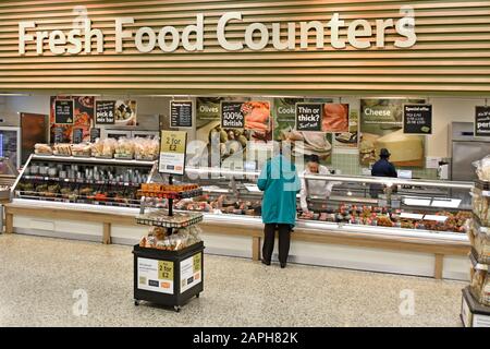 Tesco Extra Supermarktgeschäft Innenbereich Fresh Food Counter Rückansicht Frau Käufer Kunde wird am frühen Morgen serviert Fleischprodukte London England Großbritannien Stockfoto