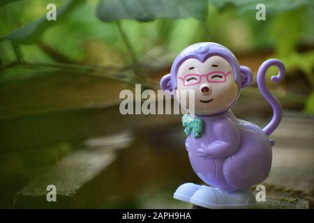 Porträt eines lächelnden Affenspielzeugs mit grünlichem Hintergrund und verschwommenen Blättern Stockfoto