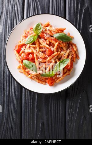 Leckere Trofie mit Tomatensauce, Käse und Basilikum in einem Teller auf dem Tisch. Vertikale Draufsicht von oben Stockfoto