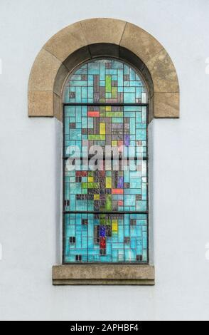 Farbige Glasfenster einer Kirche kontrastieren mit dem reinen Weiß der Wand Stockfoto