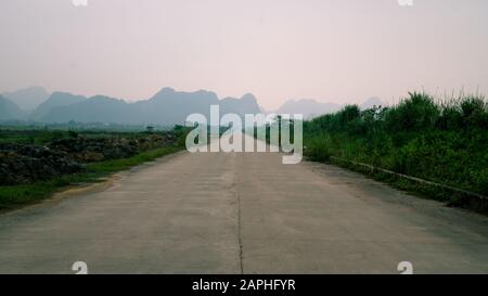 Leere Landstraße mit Kalkkarstgebirge in Ninh Binh, Vietnam an einem dunstigen Tag. Stockfoto