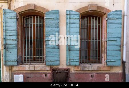 Detail der Fassade des Hauses mit schäbigen blauen Fensterläden gegen ein altes Gebäude mit Fensterleisten in Arles, Provence. Frankreich Stockfoto