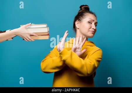 Mädchen lehnt Bücher ab, die eine weibliche Hand ihrem, nahestehenden, blauen Hintergrund aushält Stockfoto