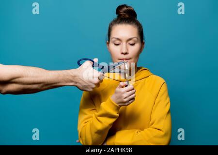 Ein Mädchen in heller Kleidung wird eine Zigarette anzünden, aber eine männliche Hand mit einer Schere wird sie aus nächster Nähe stoppen Stockfoto