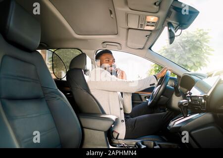 Schwarzer, gutaussehender Geschäftsleute, der das Auto fährt und auf dem Smartphone spricht Stockfoto