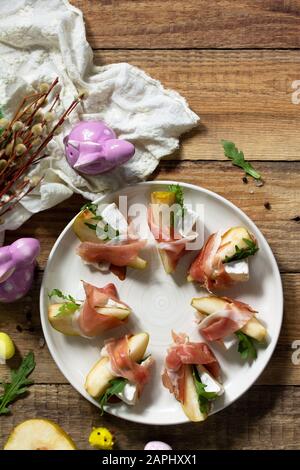 Festliche Snacks. Birnen-Vorspeise mit Jamon, Arugula und brie-käse auf einem rustikalen Holztisch. Flacher Laienhintergrund in der Draufsicht. Kopierbereich. Stockfoto