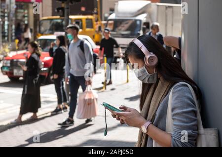 Eine Frau bedeckt ihr Gesicht mit einer sanitären Maske, als sie auf der Straße Musik hört, nachdem die ersten Fälle von Coronavirus in Hongkong bestätigt wurden. China hat ein öffentliches Verkehrsnetz und eine Flughafensperre in verschiedene Städte eingeführt, um die Ausbreitung des Wuhan Coronavirus zu verlangsamen. Stockfoto