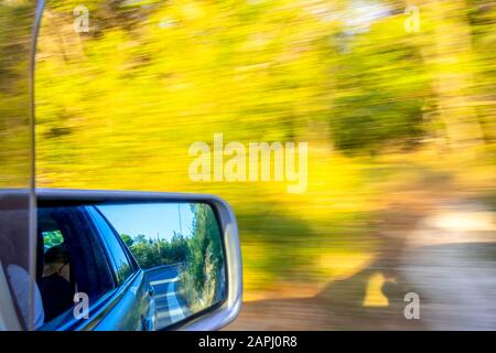 Auto geht schnell auf einer Sommerstraße. Straßenmarkierung und Buchsen im Rückspiegel. Sonniges Wetter Stockfoto