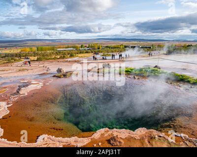 Blauer Pool mit Dampf in der Erdwärme Haukadalur mit Strokkur großem Geysir-Dampf im Hintergrund. Eine der meistbesuchten und ikonischen Sehenswürdigkeiten Stockfoto