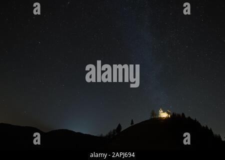 Katholische Kirche auf dem Hügel mit sichtbarer Milchstraße im Hintergrund. Religion, Astronomie und Fotografie. Stockfoto