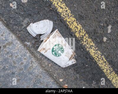 Zerkleinerte Starbucks Kaffeetasse (Papier) mit Kunststoffdeckel in der Londoner Straßenrinne. Zum Mitnehmen von Lebensmittelverpackungen, Kunststoff-Abfall, urbaner Müll. Stockfoto