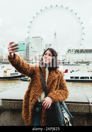 Junge Frau, die ein selfie mit dem London Eye im Hintergrund nimmt Stockfoto