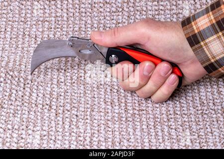 Menschen in handwerklichen Jobs. Die Hand eines Handwerkers schneidet einen Teppich mit einem professionellen Werkzeug zum Verlegen von Bodenbelägen. Makrofoto. Stockfoto