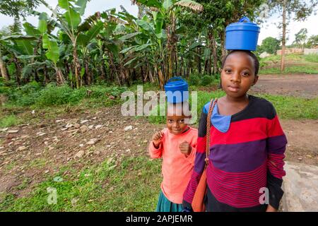 Kinder, die ihre Lebensmittelbehälter auf dem Kopf tragen, in Kitwa, Uganda Stockfoto