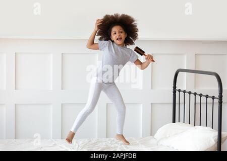 Mädchen springt auf dem Bett und hält Haarbürste wie Mikrofon und Gesang Stockfoto