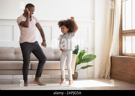 Im Wohnzimmer tanzt afrikanischer Vater mit kleiner Tochter Stockfoto