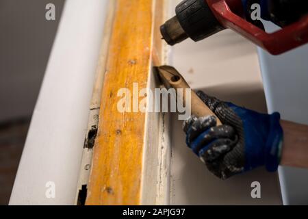 Details zum Entfernen alter weißer Farbe aus dem Türrahmen mit Heißluftpistole und Abstreifer Stockfoto