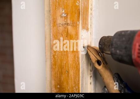 Details zum Entfernen alter weißer Farbe aus dem Türrahmen mit Heißluftpistole und Abstreifer Stockfoto