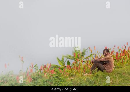 Der Mann aus Batwa-Stamm, auch Pygmäen genannt, sitzt alle alleine in der Natur, am Bunyonyi-See, in Uganda Stockfoto