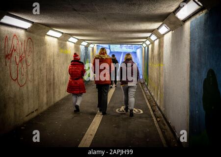 Drei Frauen in Winterkleidung, die nebeneinander unter einer Unterführung oder einer Fußgänger-U-Bahn spazieren gehen Stockfoto