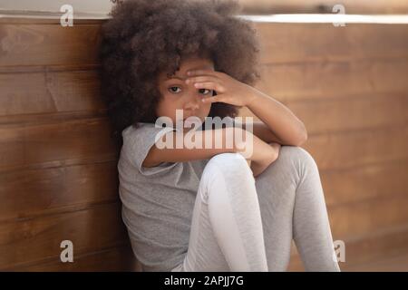 Trauriges afrikanisches Mädchen, das auf dem Boden sitzt, fühlt sich einsames Nahbild an Stockfoto