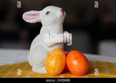 Bunte und fröhliche Osterdekorationen auf einem Tisch. Nahfarbenbild einer keramisch weißen Osterhase und bunt bemalten Ostereiern. Stockfoto