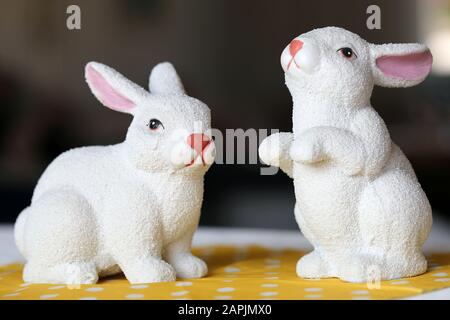 Bunte und fröhliche Osterdekorationen auf einem Tisch. Nahaufnahme des Farbbildes von zwei keramischen Osterbühnenfiguren und buntem gepunkteten gelben Tischtuch. Stockfoto