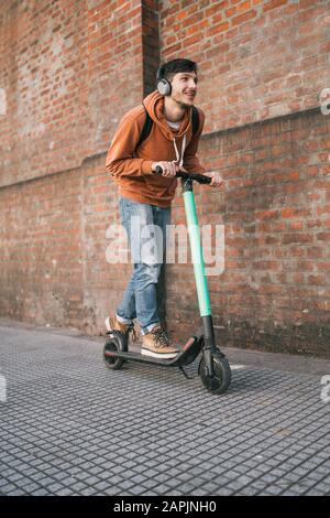 Porträt des jungen lateinmannes, der auf der Straße der Stadt einen Elektroscooter fährt. Modernes und ökologisches Transportkonzept. Stockfoto