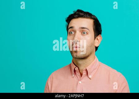 Porträt eines jungen erwachsenen Mannes, der lustige Gesichter macht, isoliert auf blauem Studiohintergrund Stockfoto