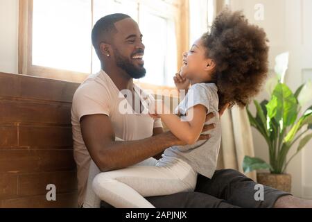 Afrikanischer Vater kitzelt kleine Tochterfamilie, die Spaß im Haus hat Stockfoto