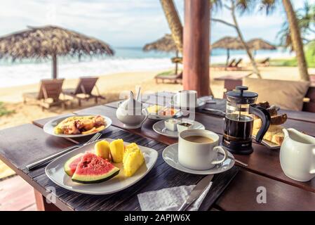 Frühstück am Strand in Sri Lanka. Tischeinstellung mit veganer Küche und Kaffee im Restaurant im Freien. Buffet mit exotischen Früchten an der Küste des Ozeans. Konzept Stockfoto