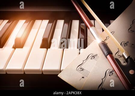 Schleife mit Noten auf Klaviertasten oben. Konzept der Interpretation von Klaviermusik und Streichinstrumenten. Vorderansicht. Horizontale Zusammensetzung. Stockfoto