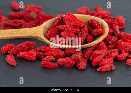 Goji-Beeren schließen getrocknete rote Beere in Holzlöffel auf grauer Schieferplatte Stockfoto