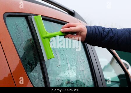 Orangefarbenes Autofenster reinigen. Autofenster mit grünem Mopp waschen. Tropfen auf Glas. Stockfoto