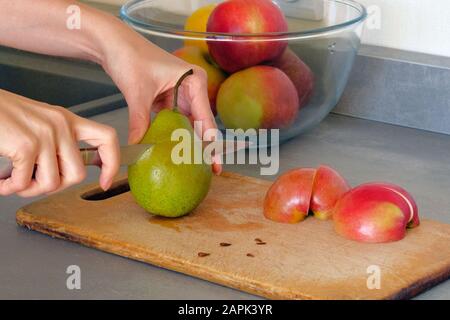 Kochkonzept. Birnen und Äpfel schneiden sich auf Holzplatten auf dem Küchentisch zu Scheiben. Stockfoto