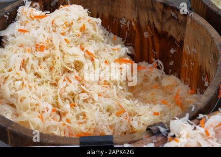 Fermentiert konserviertes vegetarisches Konzept für gesundes Essen. Sauerkraut mit orangefarbenen Karotten in Holzcontainer wird auf dem lokalen Markt nach Gewicht verkauft. Stockfoto