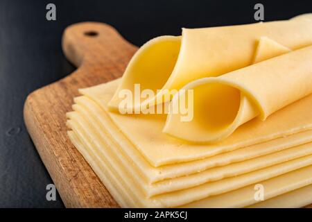 Scheiben von Gelbkäse auf einem Holzbrett. Essen vom Markt auf dem Küchentisch. Dunkler Hintergrund. Stockfoto