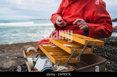 Nahaufnahme eines Fischers, der Köder mit Angelausrüstungskasten anlegt. Angel- und Sportkonzept. Stockfoto