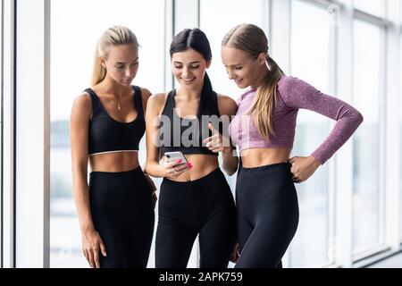 Drei Freunde, die nach dem Training im Fitnessstudio das Smartphone gemeinsam betrachten. Fitness, Sport, Freundschaft und Lifestyle-Konzept. Stockfoto