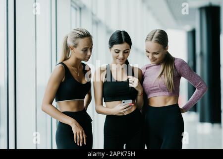 Drei Freunde, die nach dem Training im Fitnessstudio das Smartphone gemeinsam betrachten. Fitness, Sport, Freundschaft und Lifestyle-Konzept. Stockfoto