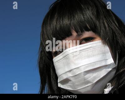 Nahaufnahme des Porträts der jungen Frau in medizinischer Schutzmaske auf blauem Himmel Hintergrund Stockfoto