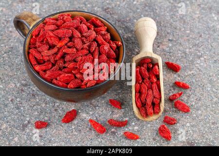 Becher und Holzlöffel mit getrockneten roten Goji-Beeren auf grauem Steingrund. Draufsicht Stockfoto