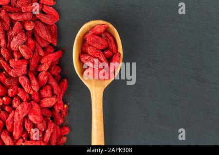 Goji-Beeren. Löffel mit organischer Beere über grauem Schieferhintergrund Stockfoto