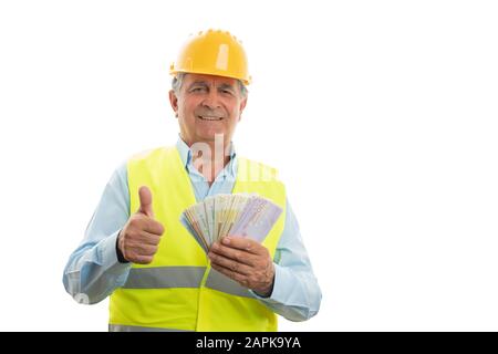 Glücklicher alter Ingenieur, der Geld hält und den Daumen nach oben zeigt, wie Geste isoliert auf weißem Studiohintergrund Stockfoto