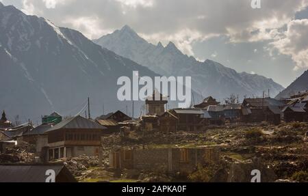 Der alte Holztempel und die Häuser des Dorfes Chitkul liegen vor dem Hintergrund der hohen schneebedeckten Berge des Himalayas, die sie umgeben Stockfoto