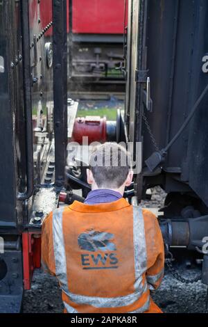Rückansicht des Mannschaftsmitglieds der Dampfzüge, Arbeiter, die alte britische Lok mit dem Eisenbahnwagen verbinden, auf der Strecke am Bahnhof Severn Valley Heritage. Stockfoto