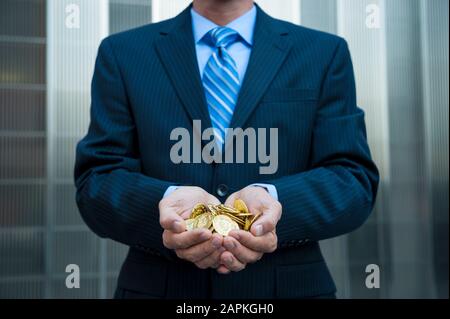 Unerkennbarer Geschäftsmann, der eine goldene Handvoll Goldmünzen im Freien in einem dunklen Anzug vor einem modernen Geschäftshintergrund hält Stockfoto