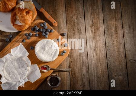 Camembert-Käse, Blaubeeren, Marmelade und Croissant auf Holzgrund Stockfoto